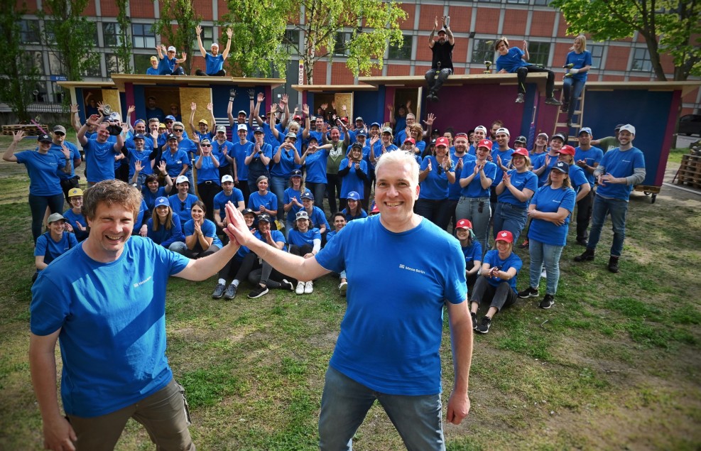 Messe Berlin employees stand in front of five Tiny Houses. In the foreground: High 5 by Dirk Hoffmann, Managing Director Messe Berlin and Sven Lüdecke, Little Home e.V.