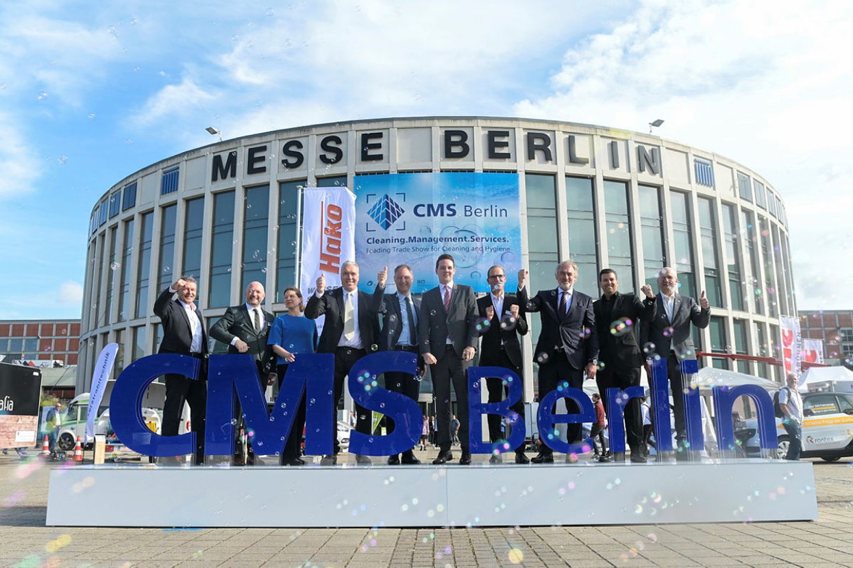 Mario Tobias und Dirk Hoffmann zusammen mit VertreterInnen der CMS stehen nebeneinander auf einem Podest mit dem Schriftzug CMS Berlin vor dem Eingang Süd. Seifenblasen überall.